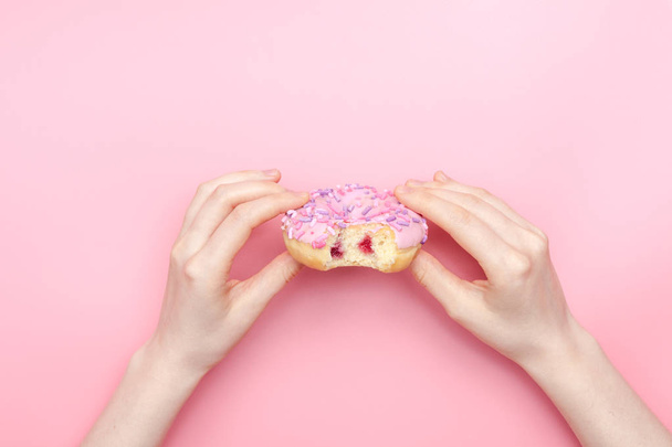 girl holding a glazed pink donut on a pink monochromatic backgro - Foto, Bild