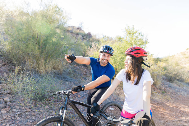Happy man pointing away while showing direction to woman while mountain biking - Photo, Image