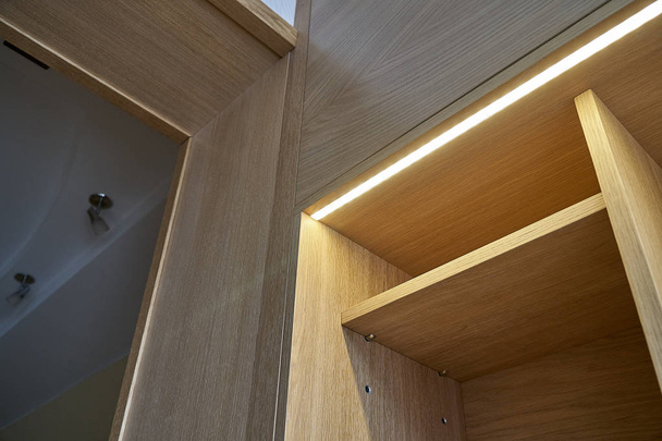 Wooden cupboard with drawers, empty shelves and LED lights. Modern furniture - Foto, imagen