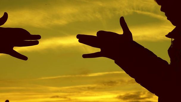 Lapset tekevät koiran muodon kädet auringonlaskun aikaan. Tytöt pitävät koiran symbolin elettä sormet taivasta vasten. lapset näyttävät käsillä eläimen siluettia. varjo pelata
 - Valokuva, kuva