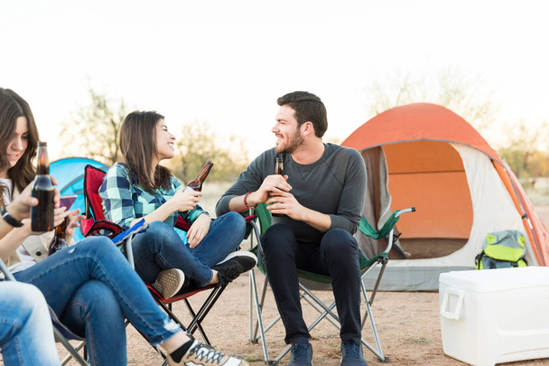 Hymyilevä ja rakastava mies ja nainen katselevat toisiaan pitäen olutpulloa teltan ulkopuolella
 - Valokuva, kuva
