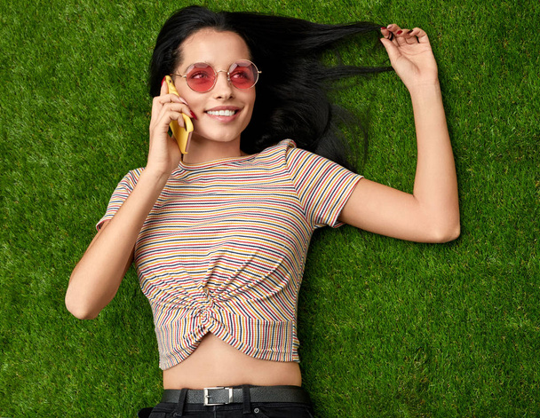 Woman speaking on phone and touching hair on lawn - Foto, Imagem