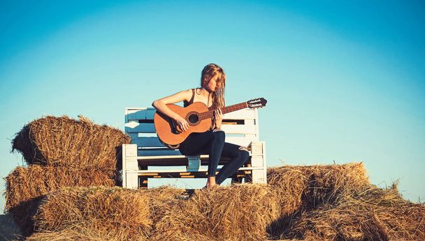 Guitar player on wooden bench on blue sky. Guitar performer hold string instrument on sunny nature - Foto, Bild