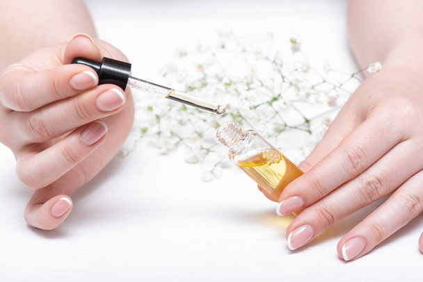 Yellow cuticle oil bottle and a female hands on a white wooden table background. Fingernail care concept. - Foto, Imagem