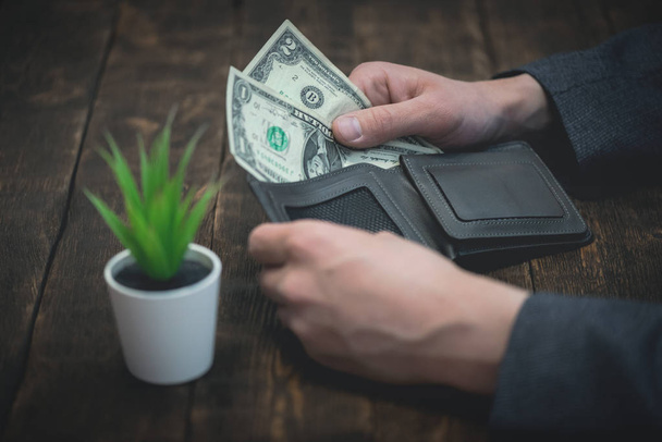 Business man is holding in hands a empty wallet with few dollars. Tight of money. Lack of money. Financial problems. Bankrupt. Pay the bill concept. - Foto, Imagem