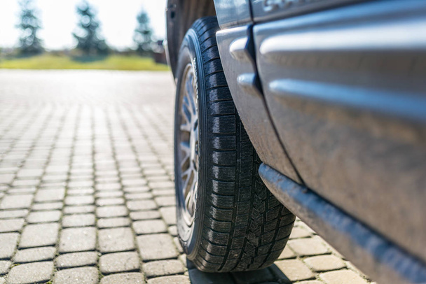 Rueda de coche con un neumático de invierno en un coche todoterreno, de pie sobre una piedra de pavimentación. Jardín casero en el fondo
. - Foto, imagen