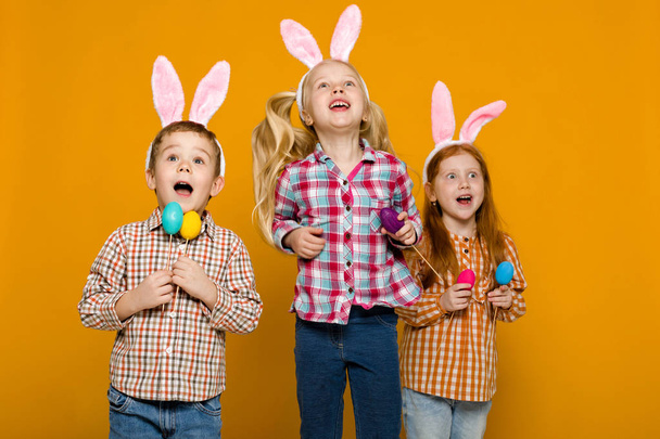 two little girls and boy with Easter bunny ears holding colorful eggs - Foto, Bild