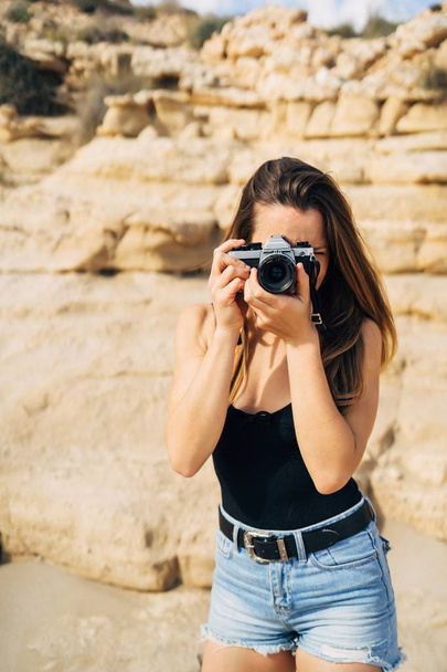Attractive young woman making photos on her vintage camera on the beach during summer vacation - 写真・画像