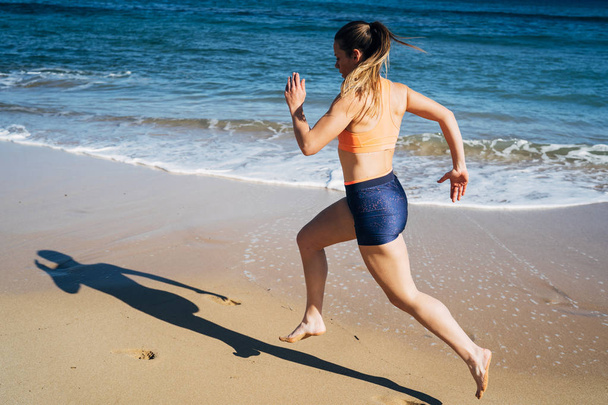 Γυμναστική νεαρή γυναίκα τρέχει στην παραλία κατά τη διάρκεια των καλοκαιρινών διακοπών - Φωτογραφία, εικόνα