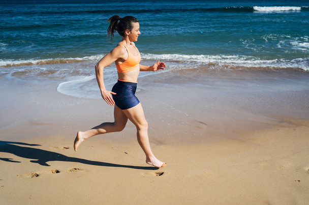 Fitness young woman running on the beach during summer holiday - Foto, imagen