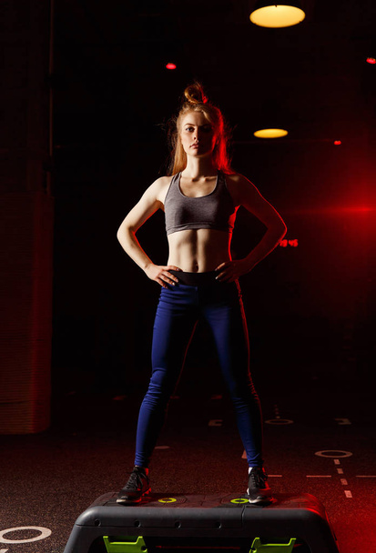 Athletic blonde standing near fitness step on black background - Foto, immagini