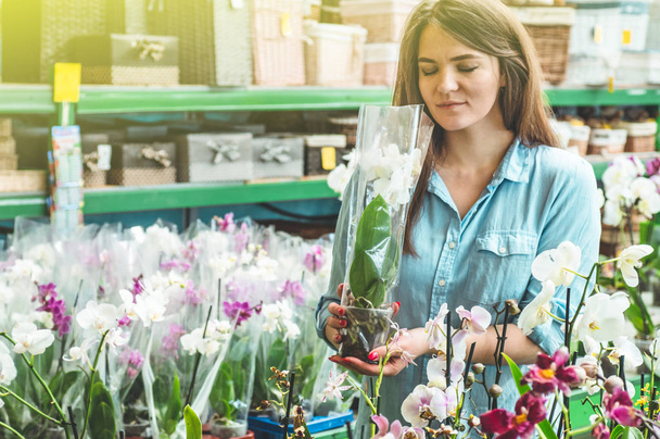 Красива жінка-клієнт пахне барвистими квітучими орхідеями в роздрібному магазині
.  - Фото, зображення