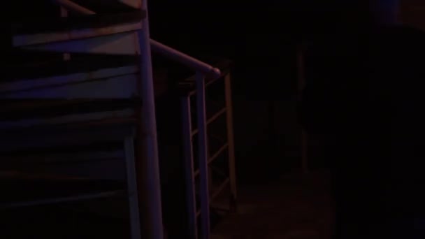 Ένας άντρας περνάει από τις κυκλικές σκάλες. Έρχεται στη γωνία του σπιτιού. Νύχτα. Σπίτι στο νερό, νυχτερινές λάμπες. - Πλάνα, βίντεο