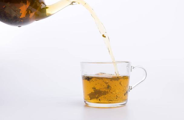 Glass teapot pouring green tea into cup isolated on white background - Φωτογραφία, εικόνα