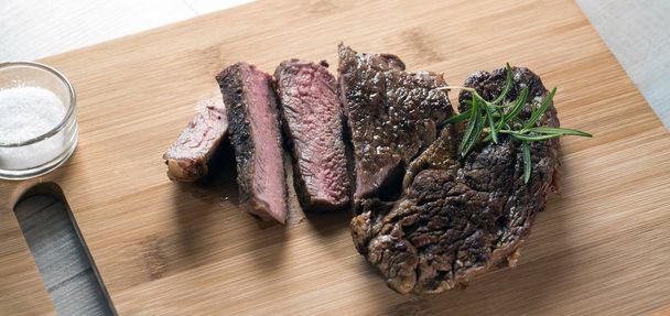 Appetizing sliced steak on chalkboard with herbs, salt and oil - Foto, Bild