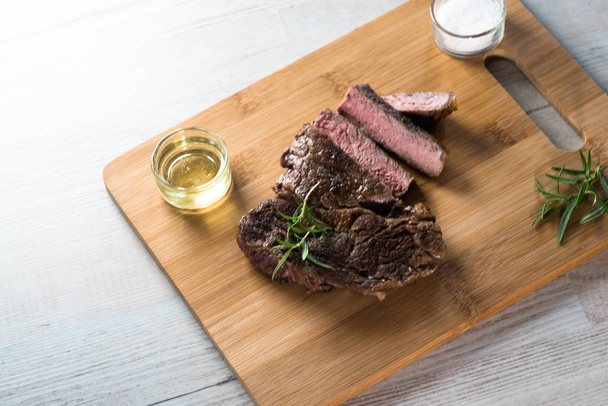 Appetizing sliced steak on chalkboard with herbs, salt and oil - Photo, image