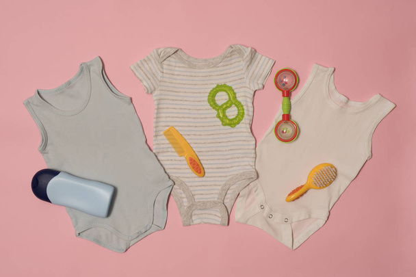 Tres body de bebé y accesorios de cuidado sobre un fondo rosa. Concepto de ropa
 - Foto, imagen