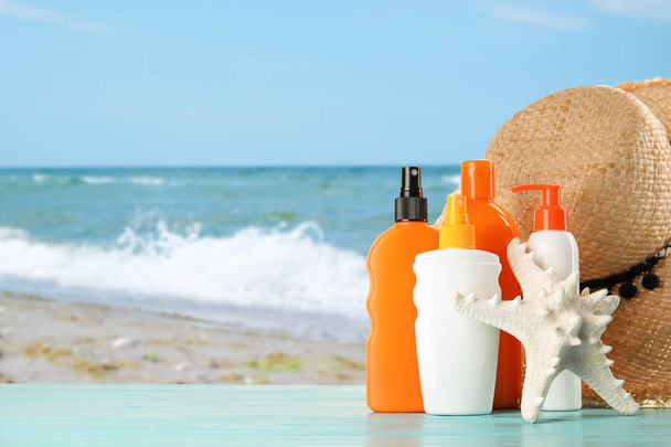 Set with different bottles of sun protection body cream and hat on wooden table against seascape. Space for design - Foto, afbeelding