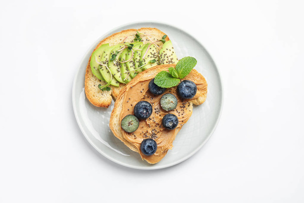 Plate of tasty toasts with avocado, blueberries and chia seeds on white background, top view - 写真・画像