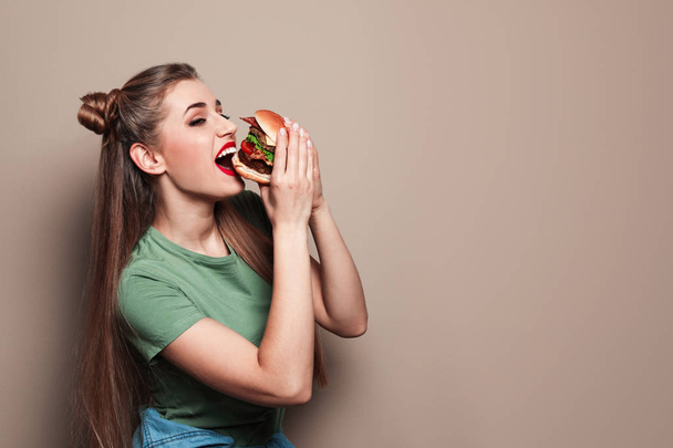Pretty woman eating tasty burger on color background. Space for text - Foto, afbeelding
