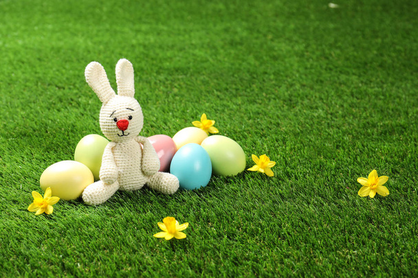 Cute Easter bunny toy and dyed eggs on green grass, space for text - Foto, imagen