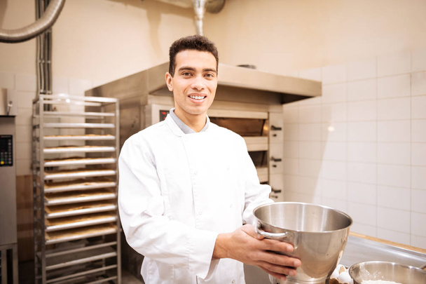 Giovane uomo dagli occhi scuri sentirsi felice di lavorare in una bella panetteria
 - Foto, immagini