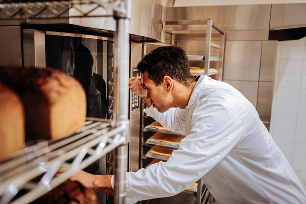 Baker looking into the glass of oven while checking eclairs - 写真・画像