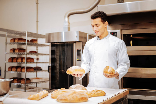 Dark-haired satisfied baker holding two loafs of bread in his hands - Fotoğraf, Görsel
