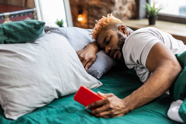 Ευχάριστη υπνηλία άνθρωπος ξαπλωμένη στο κρεβάτι με το τηλέφωνό του - Φωτογραφία, εικόνα