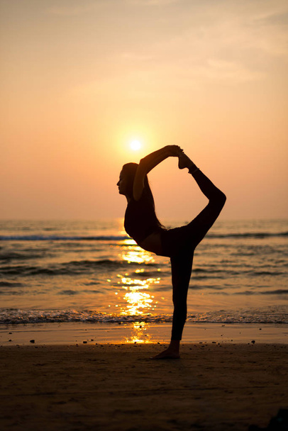 Young healthy woman practicing yoga on the beach at sunset - Fotó, kép