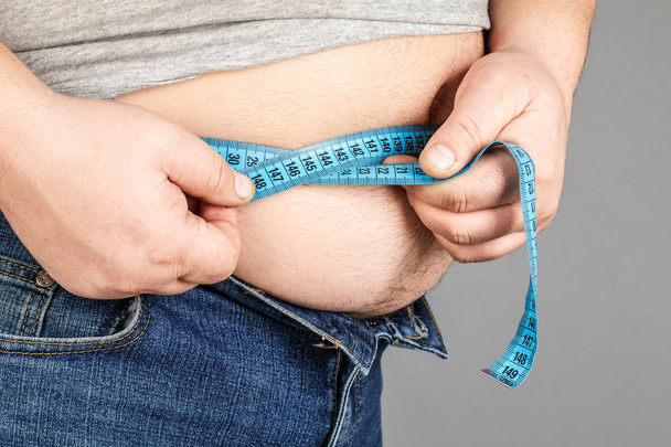 Un homme mesure son gros ventre avec un ruban à mesurer. sur une ba grise
 - Photo, image