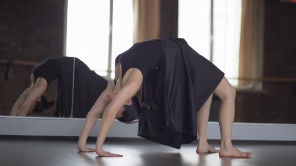 Stylish woman in black dress makes yoga asana bridge near mirror in slow motion. - Footage, Video
