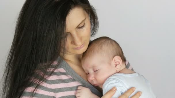 Fiatal gyönyörű Fekete hajú hosszú hajú anya két hónapos újszülött csecsemő, aki a karjában alszik. Mama bölcső neki a kisfiú - Felvétel, videó