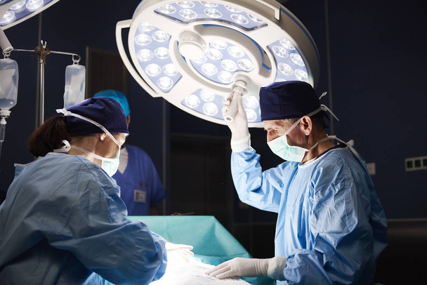 Ώριμη χειρουργός ρύθμιση το χειρουργικό φως κατά τη διάρκεια μιας λειτουργίας - Φωτογραφία, εικόνα