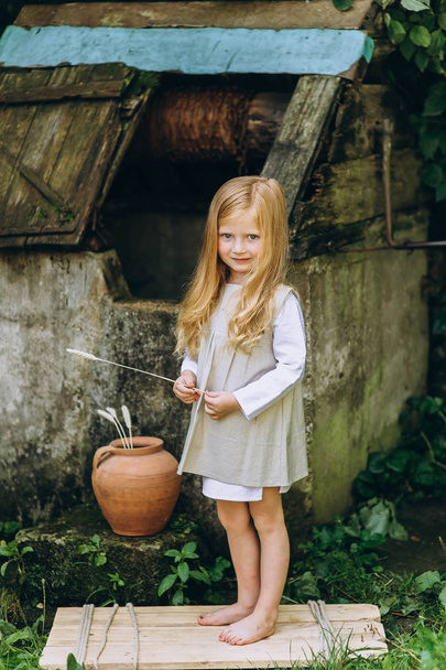 beautiful little girl with a jug and a bucket near the well on t - Φωτογραφία, εικόνα