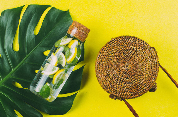Round rattan bag and glass bottle with lemonade on a Monstera le - Photo, Image