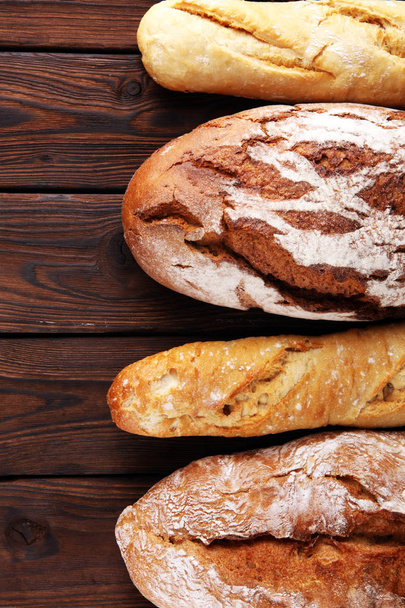 Sült kenyeret és zsemlét, a háttérben fából készült asztal - Fotó, kép