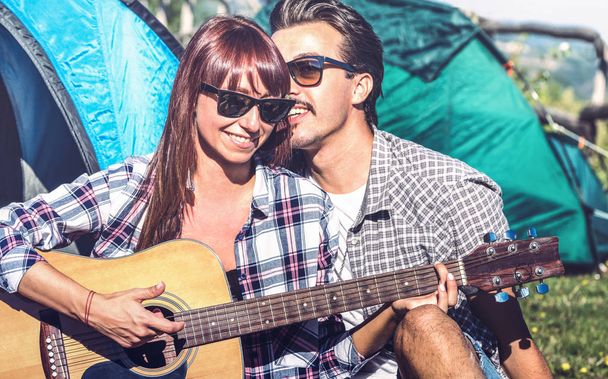 Lovers couple having fun outdoor cheering at camping place with vintage guitar - Young people enjoying summer time together in countryside - Youth travel friendship concept - Bright vintage filter - Foto, imagen