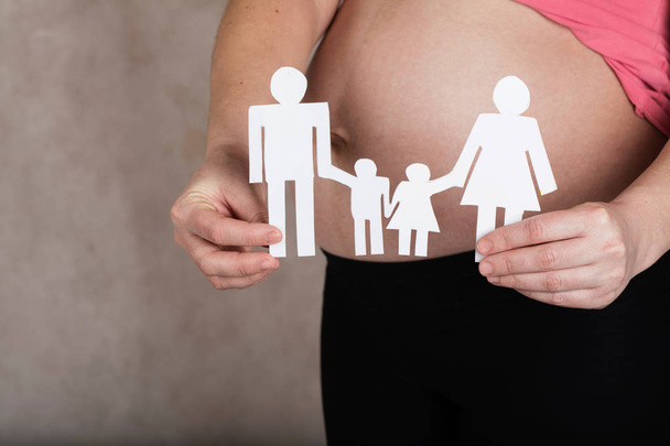 Nuori raskaana oleva nainen pitää paperileikkeitä perheestä. lähikuva-analyysi
 - Valokuva, kuva