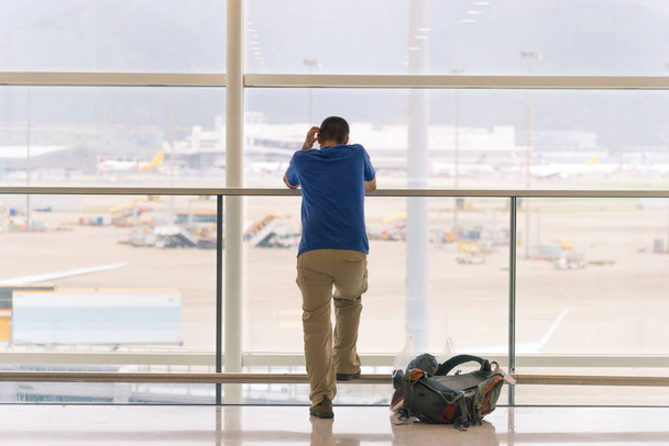 Widok z podróży człowiek stojący w pobliżu okna na Lotnisko terminal z backpacker na piętrze tyłu - Zdjęcie, obraz