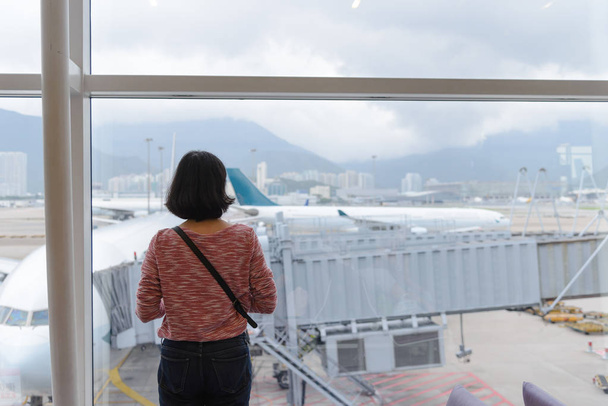 Takaisin näkymä matkustava tyttö seisoo ikkunan lähellä kansainvälisen lentokentän terminaali
 - Valokuva, kuva