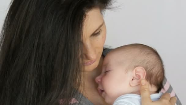 junge schöne schwarzhaarige langhaarige Mutter mit einem zwei Monate alten Neugeborenen, das in ihren Armen schläft. Mama wiegt ihren kleinen Sohn - Filmmaterial, Video