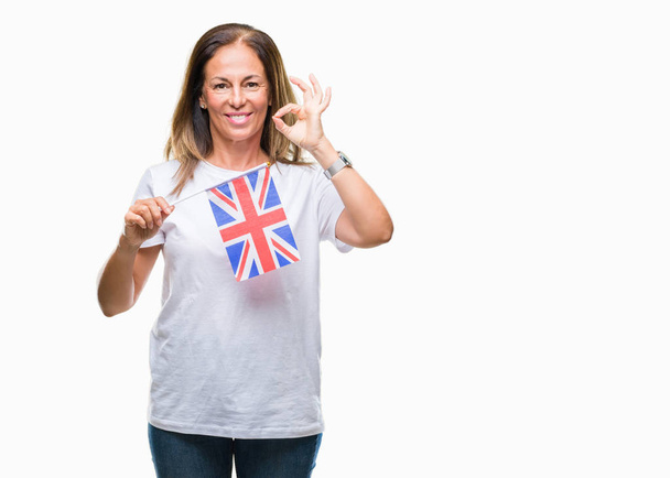 Middle age hispanic woman holding flag of United Kingdom over isolated background doing ok sign with fingers, excellent symbol - Photo, Image