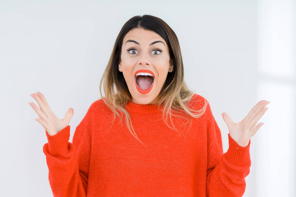 Mujer joven con suéter rojo casual sobre fondo aislado celebrando loco y sorprendido por el éxito con los brazos levantados y los ojos abiertos gritando emocionados. Concepto ganador
 - Foto, Imagen