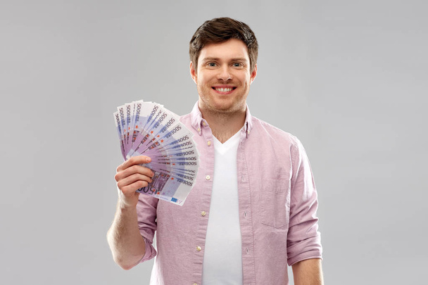 smiling young man with fan of euro money over grey - Photo, image