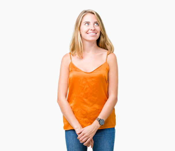 Красивая молодая женщина в оранжевой рубашке на изолированном фоне улыбается, глядя в сторону и думает:
. - Фото, изображение