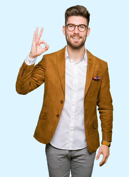 Mladý pohledný obchodní muž nosí brýle s úsměvem pozitivní jednání ok znamení rukou a prstů. Úspěšné výraz. - Fotografie, Obrázek