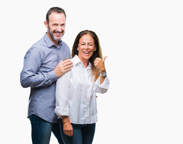 Μέση ηλικία Ισπανόφωνος επαγγελματίες ζευγάρι πέρα από το απομονωμένο υπόβαθρο χαμογελώντας με χαρούμενο πρόσωπο αναζητούν και τοποθετώντας το δείκτη στην πλευρά με τον αντίχειρα. - Φωτογραφία, εικόνα