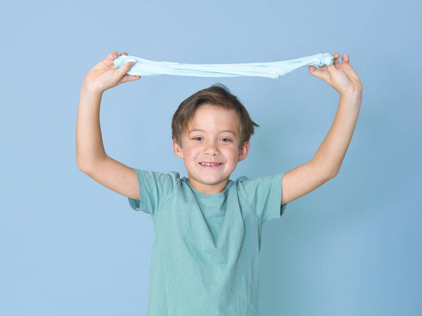 little boy plays having fun while playing with with homemade slime in front of blue background  - Foto, imagen
