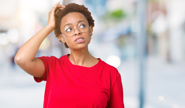 Beautiful young african american woman wearing glasses over isolated background confuse and wonder about question. Uncertain with doubt, thinking with hand on head. Pensive concept. - Photo, Image